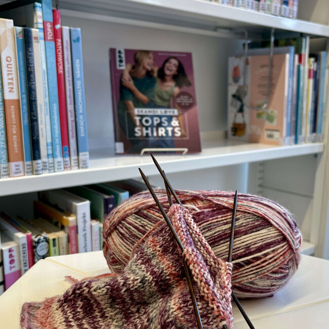 Strickprojekt mit Wollknäul vor Büchereiregal