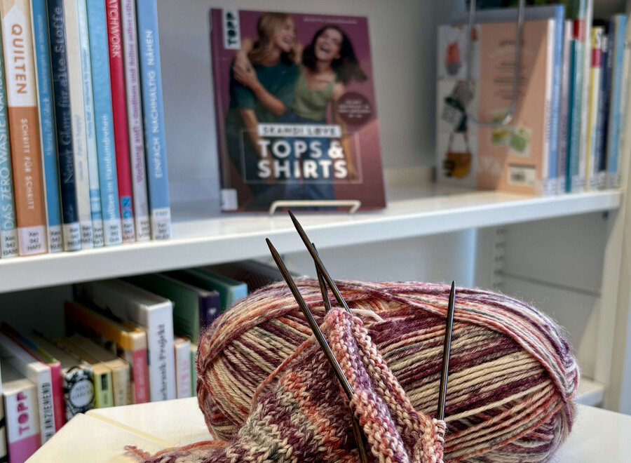 Strickprojekt mit Wollknäul vor Büchereiregal